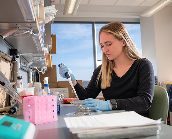 A woman in a black shirt uses a pipette at a lab desk.