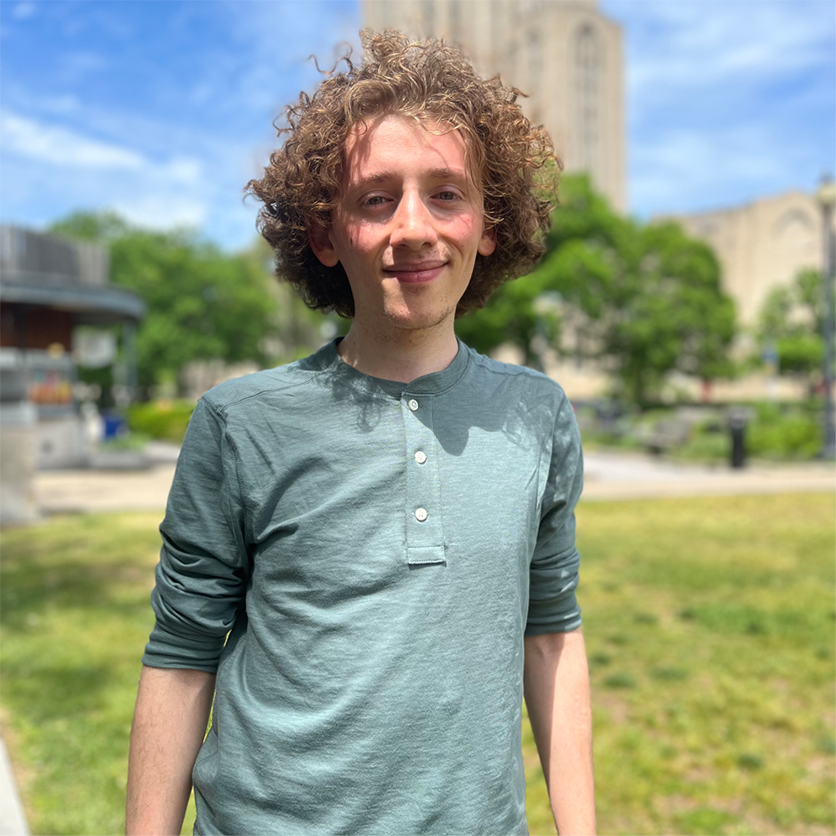 A young man in a green shirt stands in a grassy plaza.
